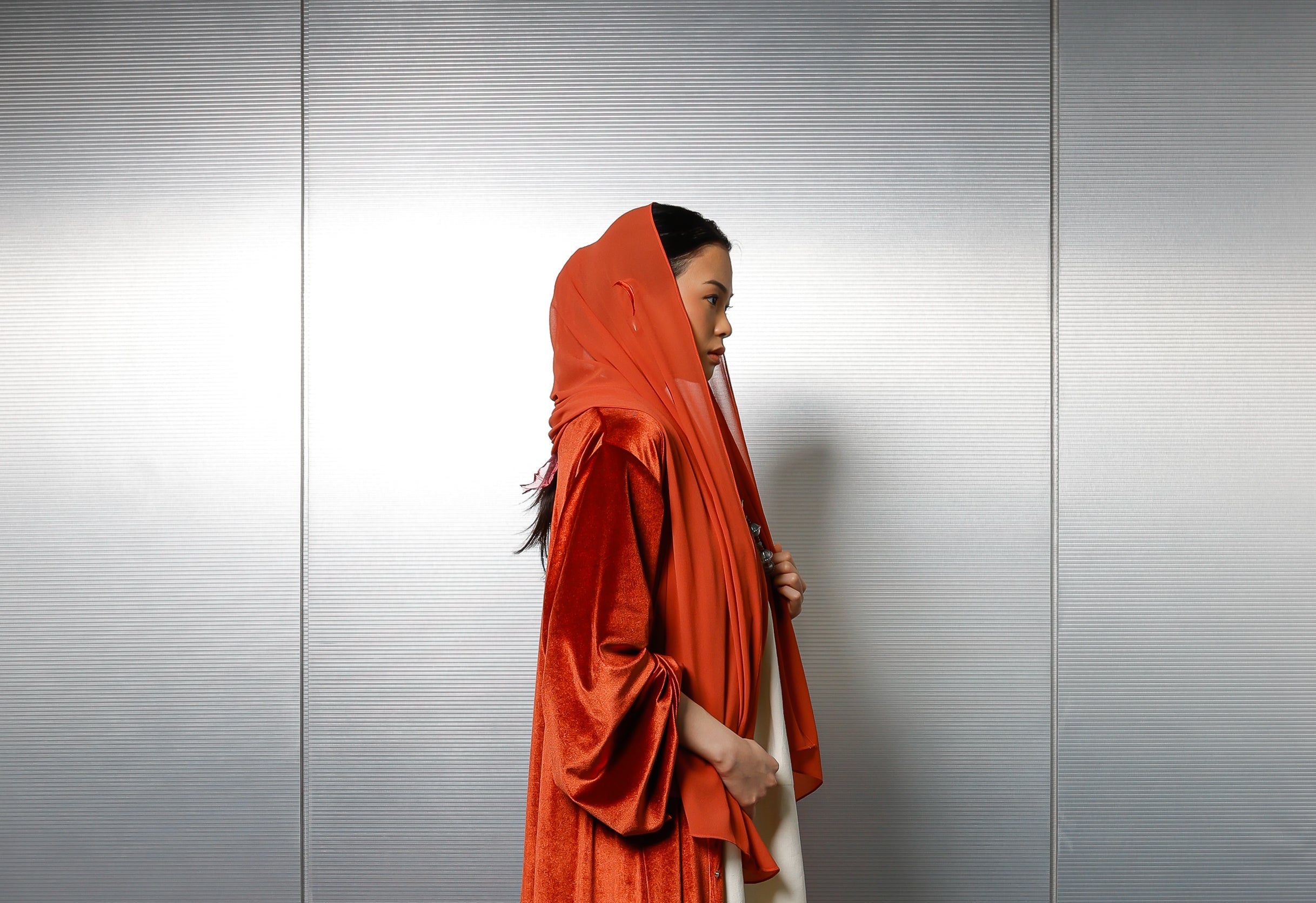 Person wearing a long orange garment against a plain background